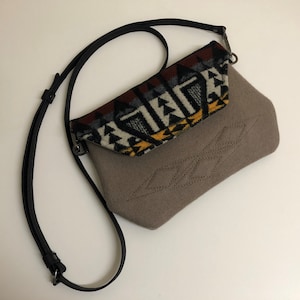 May include: A small brown crossbody bag with a black strap and a flap with a colorful geometric pattern.