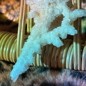 May include: A large, clear crystal formation resembling a branch, with a white, opaque center. The crystal is resting on a woven, brown surface.