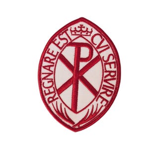 May include: A red and white embroidered patch with an oval design. The patch features a Chi Rho symbol, a crown, and the text "REGNARE EST CUI SERVIRE". The patch is set against a white background.
