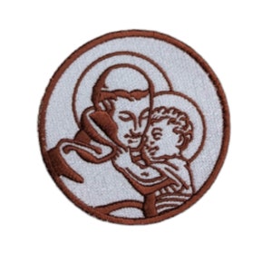 Puede incluir: Parche bordado con un contorno marrón de San Antonio de Padua sosteniendo a un bebé Jesús. El parche es circular y tiene un fondo blanco.