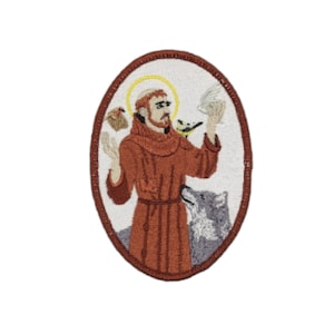 Op de afbeelding: Geborduurde patch met daarop Sint Franciscus van Assisi in een bruine robe, omringd door dieren, waaronder een wolf, een vogel en een duif. De patch is ovaalvormig en heeft een witte achtergrond.