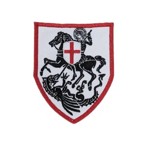 May include: A red and white embroidered patch featuring a knight on horseback slaying a dragon. The knight is wearing armor and holding a sword. The dragon is black and has wings. The patch is shaped like a shield.
