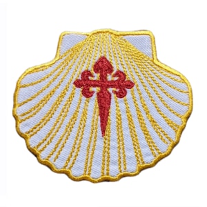 Può includere: Una conchiglia di capesante ricamata in bianco con una croce rossa e dettagli dorati. La conchiglia è un simbolo del Cammino di Santiago.