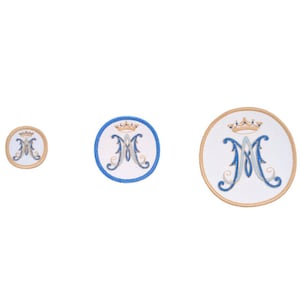 Puede incluir: Tres parches bordados con una 'M' azul y dorada con una corona encima. Los parches son circulares y tienen un fondo blanco con un borde azul. El parche más grande tiene un diámetro de aproximadamente 5 cm.