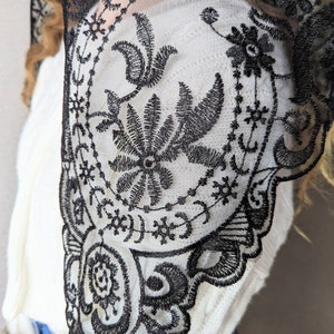May include: Black lace shawl with a floral pattern. The lace is delicate and intricate, with a scalloped edge.