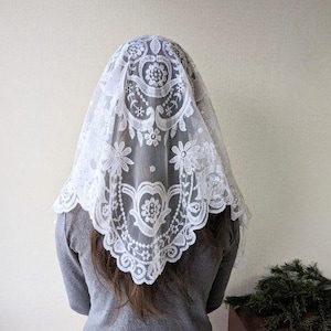 May include: White lace mantilla with a floral pattern. The lace is delicate and has a scalloped edge.