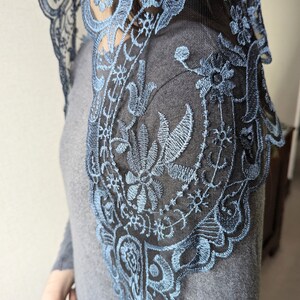 Puede incluir: Una mantilla de encaje negro con bordados azules. El encaje es delicado e intrincado, con un patr&oacute;n floral. La mantilla es un tocado tradicional que usan las mujeres en algunas culturas.