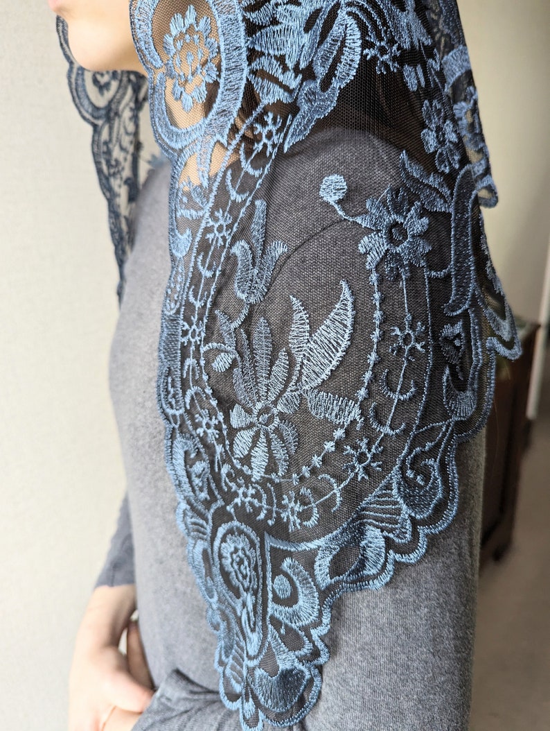Puede incluir: Una mantilla de encaje negro con bordados azules. El encaje es delicado e intrincado, con un patr&oacute;n floral. La mantilla es un tocado tradicional que usan las mujeres en algunas culturas.