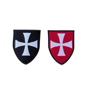 May include: Two shield-shaped embroidered patches featuring a white cross centred on each. One patch has a solid black background, while the other patch has a solid red background. Both patches are outlined with a thin black border.