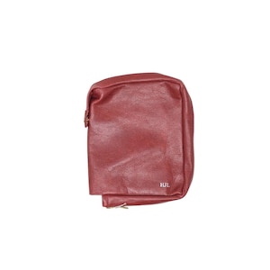 May include: A burgundy leather pouch with a rectangular shape. The pouch has a zipper closure and a small gold-colored zipper pull. The initials "HJL" are visible in the lower right corner.