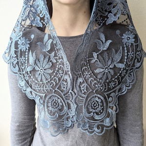 Puede incluir: Una mantilla de encaje azul claro con bordados florales. El encaje es delicado y tiene un borde festoneado.