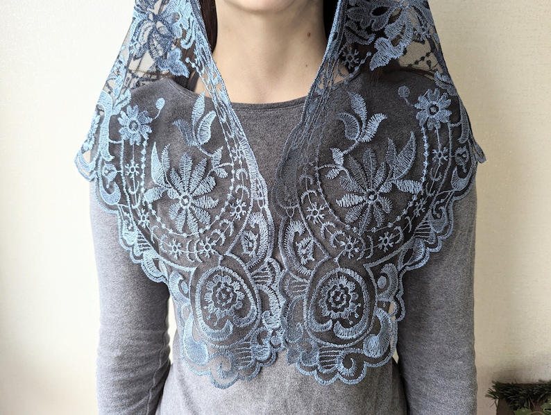 Puede incluir: Una mantilla de encaje azul claro con bordados florales. El encaje es delicado y tiene un borde festoneado.
