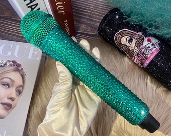 May include: A green microphone covered in sparkling emerald green rhinestones. The microphone is resting on a white satin glove.