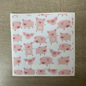 Puede incluir: Una tarjeta blanca con un patrón repetido de cerdos de dibujos animados rosas en varias poses. Algunos cerdos están de pie, otros tumbados. La tarjeta tiene dos recortes rectangulares cerca de la parte inferior. El diseño es juguetón y caprichoso.