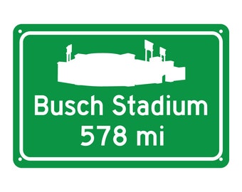 May include: Green road sign with white text and a silhouette of a stadium. The sign reads "Busch Stadium 578 mi".