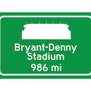 K&ouml;nnte beinhalten: Ein gr&uuml;nes Stra&szlig;enschild mit wei&szlig;em Text und einer wei&szlig;en Silhouette eines Stadions. Das Schild lautet "Bryant-Denny Stadium 986 mi".