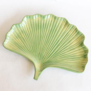 May include: A light green ceramic serving dish shaped like a ginkgo leaf. The dish features a ribbed texture and a scalloped edge. The colour is a soft, muted green with hints of yellow.