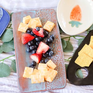 May include: A rectangular serving platter with a blue and brown glaze and a decorative pattern. The platter is filled with cubed cheese, strawberries, and blueberries.