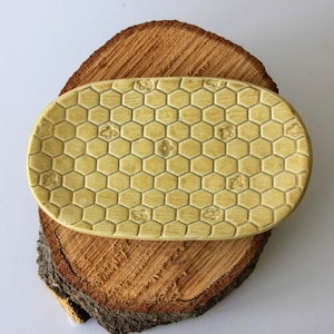 May include: A light yellow ceramic dish with a honeycomb pattern. The dish is oval shaped and has a slightly raised edge.