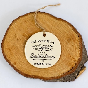 Puede incluir: Adorno de cerámica blanca con el texto "The Lord is my Light and Salvation Psalm 27:11" en letras negras.