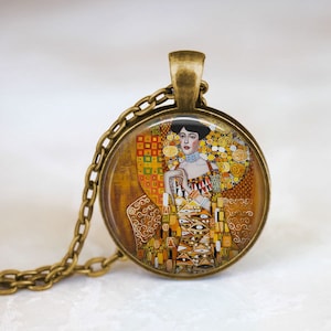 May include: A gold-toned necklace with a round glass pendant featuring a painting of a woman in a colorful dress. The painting is a reproduction of Gustav Klimt's "The Lady with the Ermine".