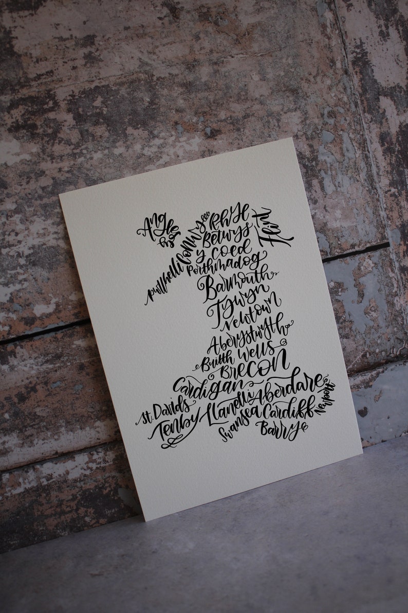 May include: A black and white illustration of the outline of Wales with the names of towns and cities in Wales written inside the outline. The names include:  Anglesey, Rhyl, Holyhead, Conwy, Betwys y Coed, Porthmadog, Barmouth, Tywyn, Newtown, Aberystwyth, Builth Wells, Brecon, Cardigan, St. Davids, Tenby, Llanelli, Aberdare, Swansea, Cardiff, Barry, Newport.