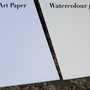 May include: Close-up of two sheets of paper, one matte art paper and one watercolor paper. The matte art paper is a light blue color and the watercolor paper is a white color.