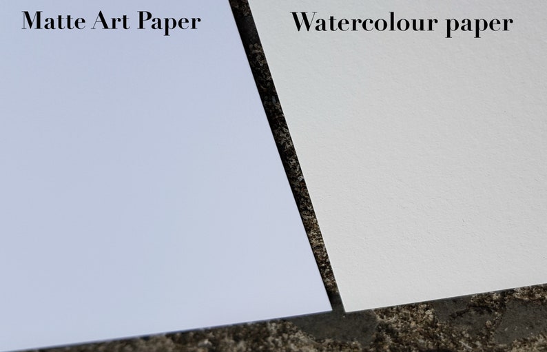 May include: Close-up of two sheets of paper, one matte art paper and one watercolor paper. The matte art paper is a light blue color and the watercolor paper is a white color.