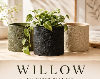 May include: Three cylindrical planters in olive green, black, and beige, each featuring a raised, repeating teardrop and dot pattern. A green leafy plant sits inside the black planter. The text WILLOW TEXTURED PLANTER is displayed below.