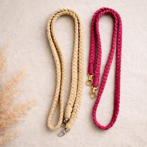 May include: Two braided rope straps in the image. One is a light beige color, and the other is a vibrant magenta. Both straps have metal clasps for attachment. The beige strap has silver-colored clasps, while the magenta strap has gold-colored clasps.