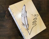Notebook with quill cut out on wooden cover. Bound with Coptic Stitching.