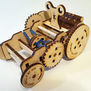 May include: A wooden toy with a key wind-up mechanism and multiple gears. The toy has a blue ribbon wrapped around a spool and the words "OXWI WHEEL P 21 mm" are printed on one of the gears.