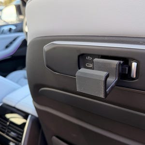 May include: A close-up of a black car interior featuring a USB port and a black plastic holder. The interior has white leather seats and a black dashboard. The car is parked outside.