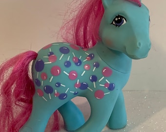 Könnte beinhalten: Ein blaues und pinkfarbenes My Little Pony Spielzeug mit einer pinkfarbenen Mähne und einem pinkfarbenen Schwanz. Das Pony hat ein Zuckerstangen- und Lutschermuster auf seinem Körper.