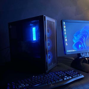 Könnte beinhalten: Ein schwarzer Computer-Tower mit blauen LED-Lichtern, eine schwarze Tastatur und ein schwarzer Monitor mit einem blauen und weißen abstrakten Design auf dem Bildschirm.