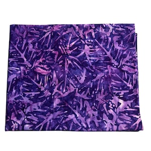 May include: A folded piece of fabric with a batik design. The fabric features a deep indigo background with a pattern of light purple, branch-like shapes. The overall effect is a textured, artistic textile, suitable for various craft projects.