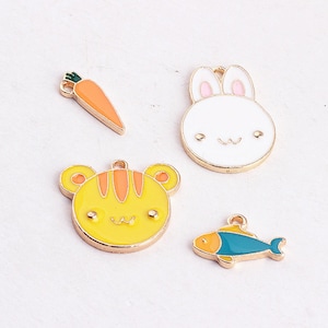 May include: Four enamel charms with gold-tone metal settings. The charms are a carrot, a bunny, a tiger, and a fish. The carrot is orange, the bunny is white with pink ears, the tiger is yellow with orange stripes, and the fish is blue and orange.