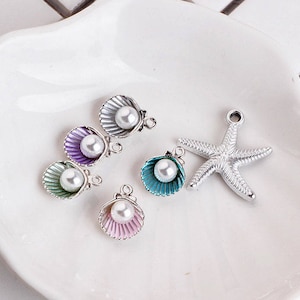 May include: Assortment of silver-toned charms featuring seashells with pearl accents in various colors, including teal, purple, and pink. A silver-toned starfish charm is also included.