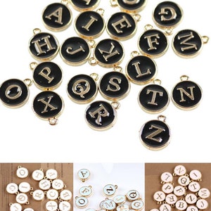 May include: Assortment of gold-colored alphabet letter charms with black enamel. Each charm features a single letter in a gold font. The charms are round and have a small loop at the top for attaching to jewelry or other crafts.
