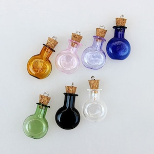 Puede incluir: Conjunto de ocho pequeñas botellas de vidrio con tapones de corcho y tapas plateadas. Las botellas son de varios colores, incluyendo transparente, ámbar, rosa, morado, negro y verde.