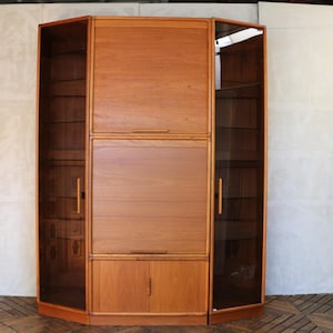 May include: A mid-century modern wooden cabinet with a light brown finish. The cabinet has a central section with a roll-top door and two side sections with glass doors. It features multiple shelves and a lower cabinet with two doors.