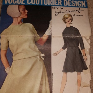 Könnte beinhalten: Vogue Couturier Design Schnittmuster 1510 von John Cavanagh aus London. Das Schnittmuster zeigt zwei Kleider, eines in hellbeige und das andere in Schwarz. Das beige Kleid hat einen kurzen Ärmel und eine Schleife in der Taille. Das schwarze Kleid hat einen kurzen Ärmel und eine Schleife in der Taille. Das Schnittmuster ist für ein Kleid.