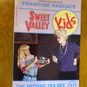 Puede incluir: Una portada de libro de la serie Sweet Valley Kids, titulada "The Missing Tea Set". La portada presenta a una niña sosteniendo una tetera de plata y a una mujer mayor con una expresión severa.