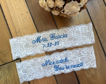 May include: Two white lace garters with blue embroidery. The top garter says "Mrs. Garcia 7-22-25". The bottom garter says "Nice catch, you're next!"