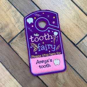 May include: Purple felt tooth fairy door hanger with a pink felt pocket that says "Please stop here for Areya's tooth".