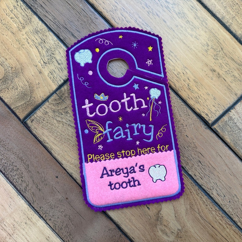 May include: Purple felt tooth fairy door hanger with a pink felt pocket that says "Please stop here for Areya's tooth".