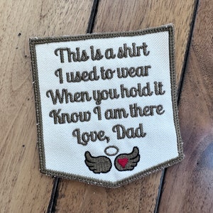 May include: A white fabric patch with brown embroidered text that reads "This is a shirt I used to wear When you hold it Know I am there Love, Dad". The patch has a pair of brown wings with a red heart in the center.