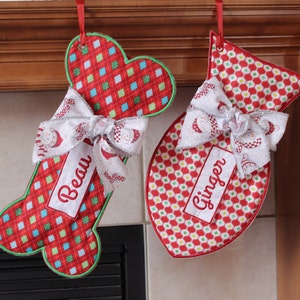 Peut inclure: Deux chaussettes de Noël rouges et vertes avec des nœuds blancs et des noms personnalisés, "Beau" et "Ginger", accrochées à une cheminée en bois.