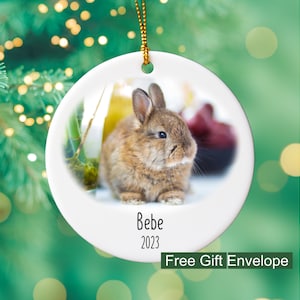 May include: A white ceramic Christmas ornament with a picture of a brown bunny rabbit. The ornament has the text "Bebe 2023" printed on it.