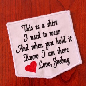 May include: White fabric patch with black embroidered text that reads "This is a shirt I used to wear And when you hold it Know I am there Love, Foebug". A red heart is embroidered below the text.